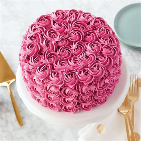 A Pink Cake Sitting On Top Of A White Plate Next To Gold Forks And Spoons