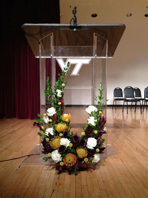 A Podium With Flowers And Greenery In Front Of A Microphone On A Wooden