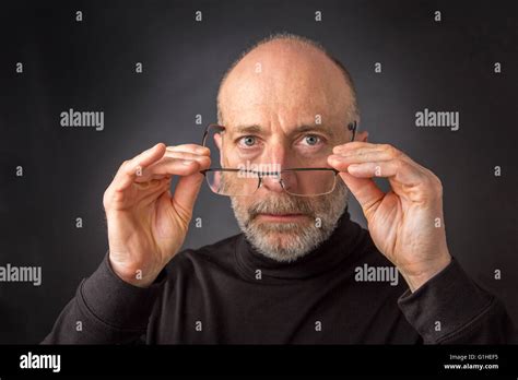 Look Over Reading Glasses Headshot Of 60 Years Old Man With A Beard Against A Black Background