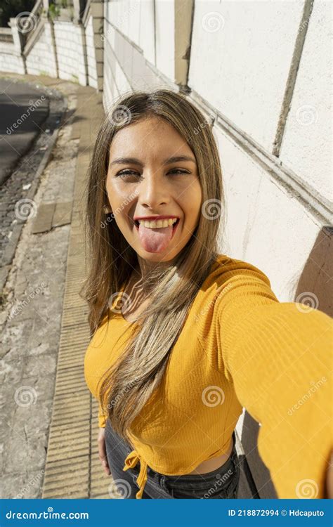 Beautiful Young Latina Sticking Out Her Tongue In A Fun Way While Taking A Selfie With Her Cell