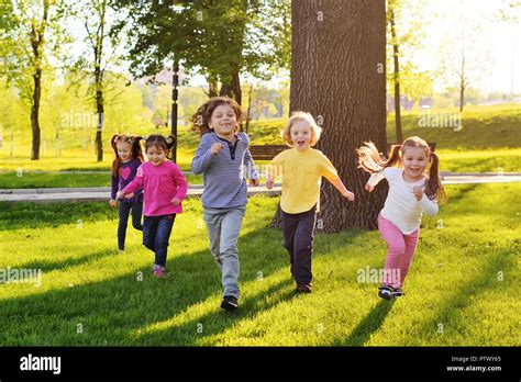 A Group Of Small Happy Children Run Through The Park In The Background