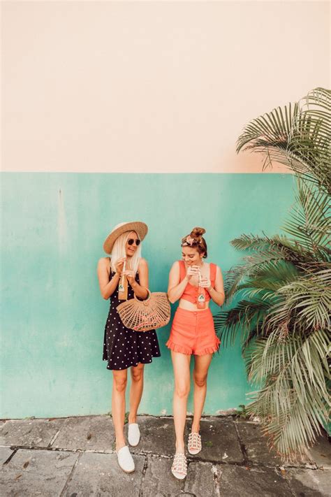 Two Women Standing Next To Each Other In Front Of A Blue Wall And Palm Tree
