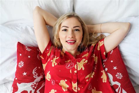 Beautiful Blonde Girl In Red Pajamas Lies On The Bed Smiles And Looks