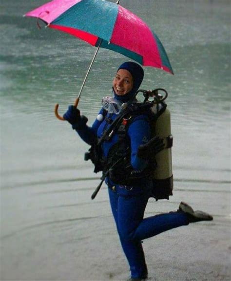 A Woman In Blue Wetsuit Holding An Umbrella Over Her Head While Standing On The Beach