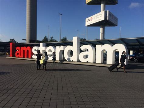 Two People Walking Past A Large Sign That Says I Am Amsterdam In Front