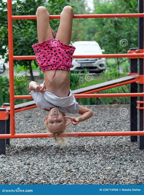 Girl Years Old Is Playing Cheerfully On The Playground Hanging Upside Down Stock Photo