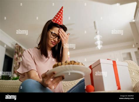 an unhappy girl wearing a hat on her birthday with a cake with candles is alone in the room