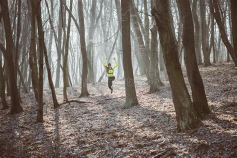 Female Athlete Running In The Forest Trail And Jumping Stock Photo