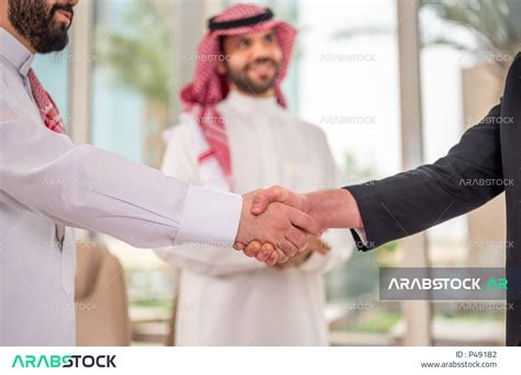 رجل اعمال عربي سعودي خليجي بالثوب السعودي التقليدي يتصافح مع عميل جديد يرتدي البدلة الرسمية