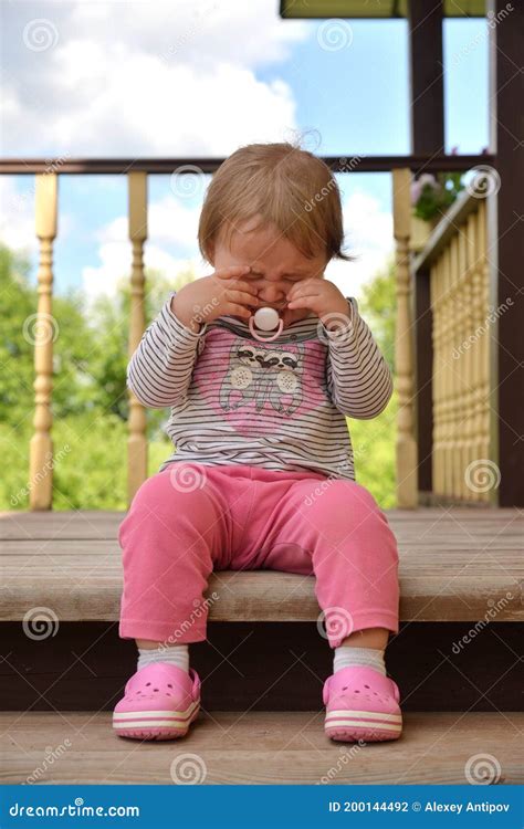 Little Girl With Pacifier Crying Sitting On Wooden Porch Stock Photo