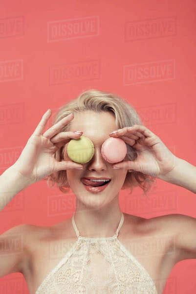 Beautiful Girl Licking Lips And Holding Two Macarons In Front Of Eyes Isolated On Red Stock