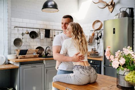 Pair Of Lovers Kissing And Hugging In Kitchen Next To The Refrigerator