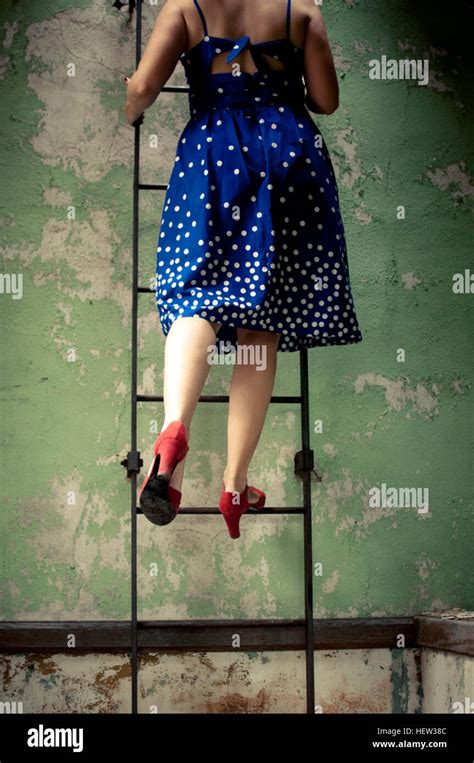 Rear View Of Woman Wearing Dress And High Heels Climbing Ladder Stock