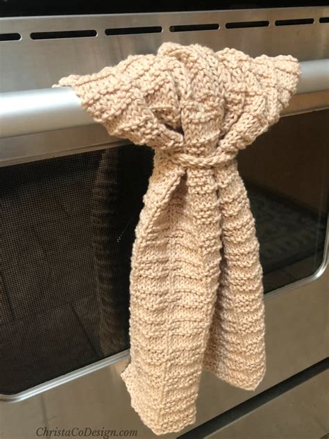 Beige Textured Knit Towel Hanging From Stainless Steel Oven Bar