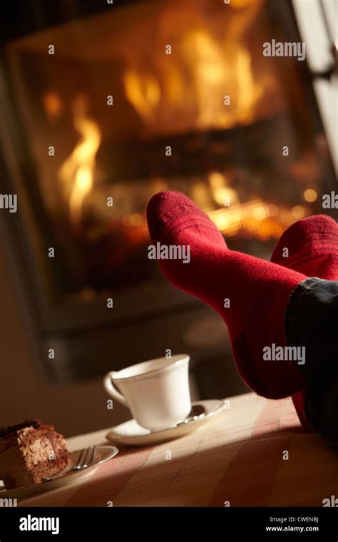 Close Up Of Mans Feet Relaxing By Cosy Log Fire With Tea And Cake Stock