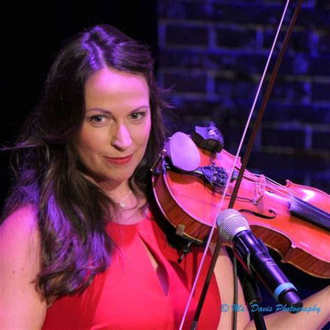 A Woman Holding A Violin And Microphone In Front Of A Brick Wall With