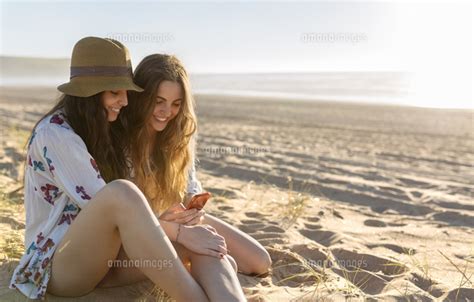 Two Best Friends Sitting On The Beach Looking At Smartphone 11094028156