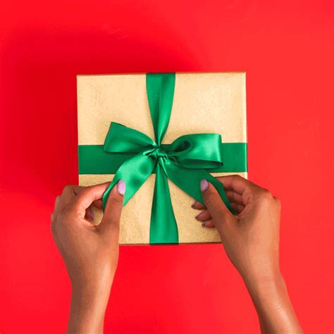 Two Hands Holding A Wrapped T Box With Green Ribbon On Red