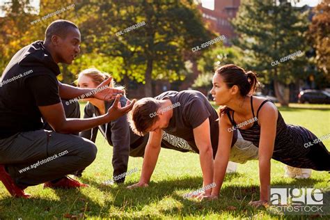 Personal Trainer Instructing Man And Women Doing Push Ups In Park