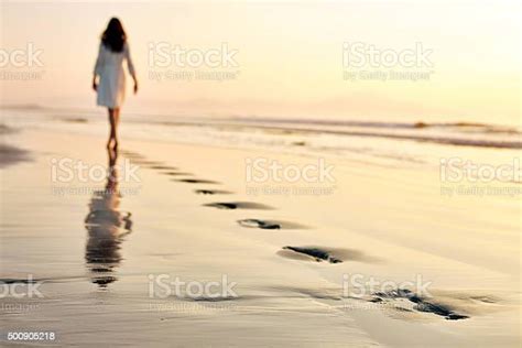 Woman Leaving Footprints While Walking On Wet Sand At Sunset Stock
