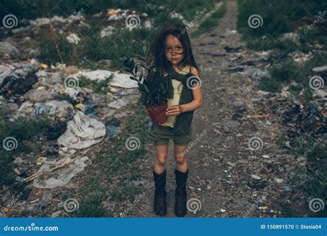 A Homeless Girl Is Standing On A Garbage Dump With A Houseplant In A