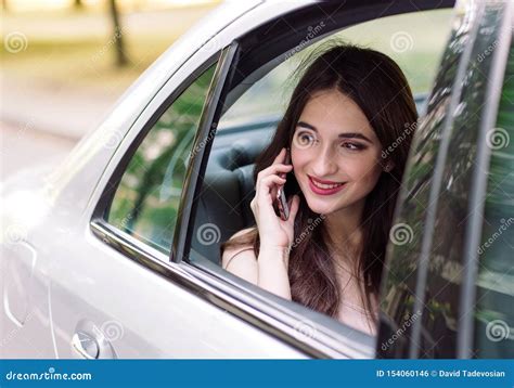 A Young Girl Is Sitting In The Back Seat Of A Car And Is Talking On The