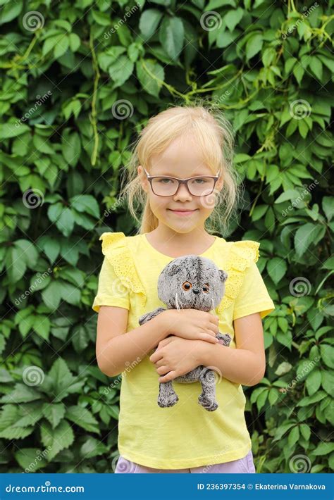Blonde Girl In Glasses And A Yellow T Shirt With A Favorite Toy Kitten