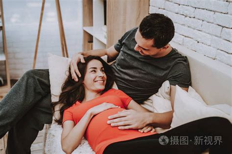 男人正在拥抱他怀孕的妻子。 妻子是个年轻的黑发女人。 丈夫是支持女人的。 夫妻幸福而微笑。 女孩在摸她的肚子。 沙发上的人。 住照片 正版商用图片150szx 摄图新视界