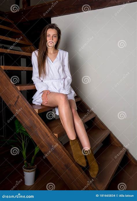 Beautiful Woman In A White Short Dress Sitting On The Stairs At Home