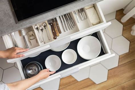 A Person Is Reaching Into A Drawer With Dishes And Utensils In It On