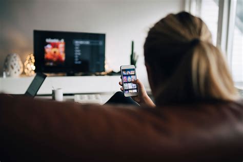 Rear View Of Teenage Girl Using Smart Phone App While Watching Tv In