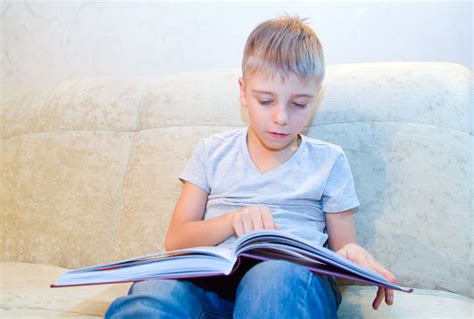 Anak Kecil Membaca Buku Duduk Di Rumah Di Sofa Krem Dan Sangat Tertarik
