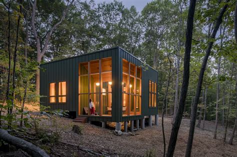 This Dark Green Cabin Floats Above A Sloping Terrain In A Forest In
