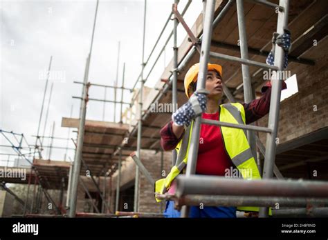 Female Construction Worker Climbing Ladder At Construction Site Stock