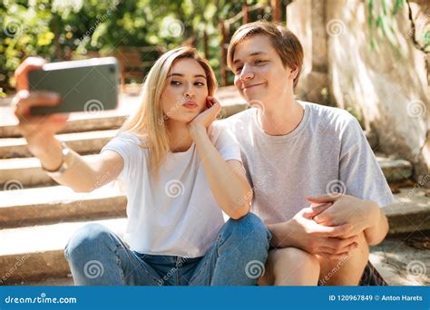 Young Couple Sitting On Stairs In Park And Making Cute Selfie Together