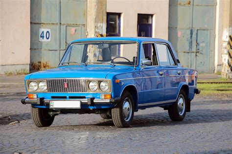 An Old Blue Car Is Parked In Front Of A Building On A Cobblestone Street