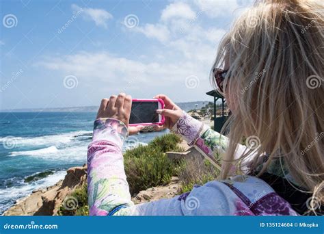 Blonde Female Takes A Photo With Smart Phone Of The Rugged Rocky Beach