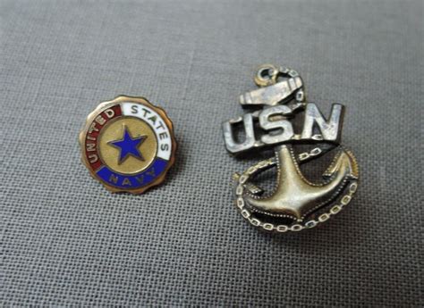 two lapel pins with the words usn and an anchor on one side sitting next to each other