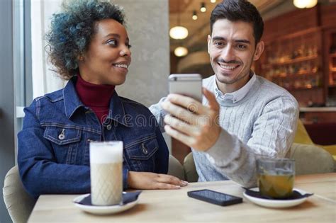 Mixed Race Couple Sitting In Cafe And Sharing New App Using Smartphone