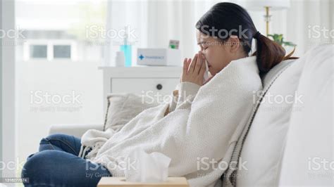 Sick Young Asian Woman Sitting Under The Blanket On Sofa And Sneeze