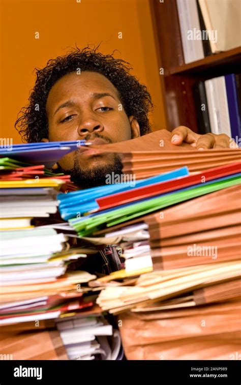 Over Worked Young Man Looking Through A Pile Of Colorful Folders On His