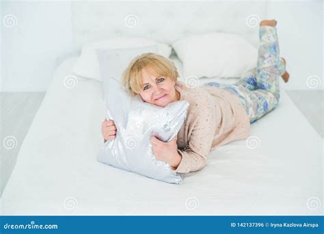 Smiling Older Woman Resting In The Bedroom Embracing Pillow Stock