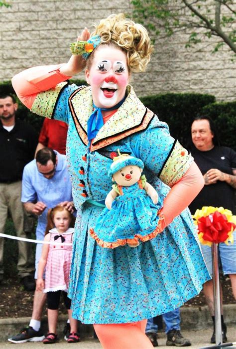 A Woman Dressed As A Clown Holding A Small Doll In Her Hand And