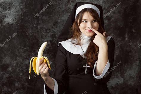 close up of a sexy nun holding a banana and cartridges thumb his nose on a dark background