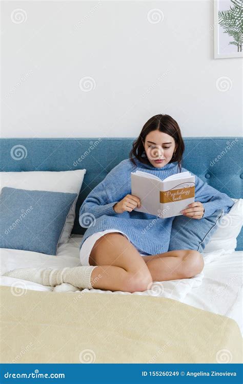 Girl In A Blue Sweater Reading A Book On Psychology Sitting On The Bed In A Cozy Interior Stock