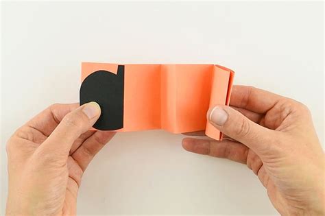 Two Hands Holding An Orange And Black Piece Of Paper