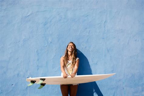 Fille Heureuse De Surfer Avec La Planche De Surf Devant Le Mur Bleu