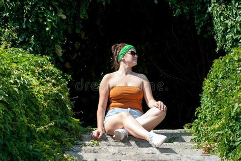 chica en pantalones cortos pantalones cortos sentada en escalones de concreto en un parque de la