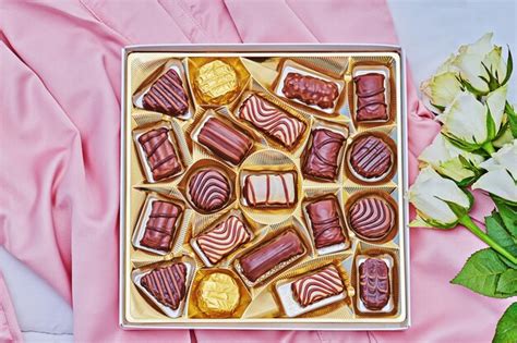 Premium Photo Golden T Box Of Assorted Chocolate On Pink Silk With White Bouquet Of Rose