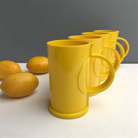 Four Yellow Mugs Sitting Next To Lemons On A White Counter Top With